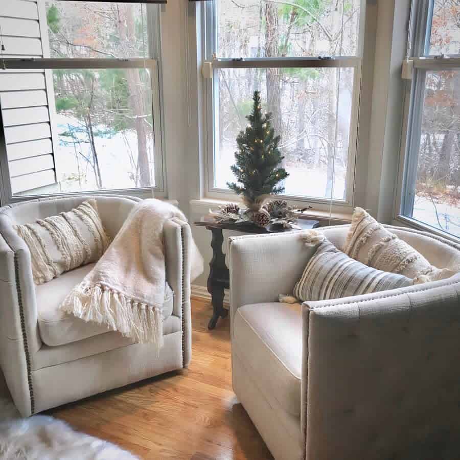 Cozy bay window nook with plush armchairs, soft throws, and a small festive tree, creating a warm and inviting winter retreat.