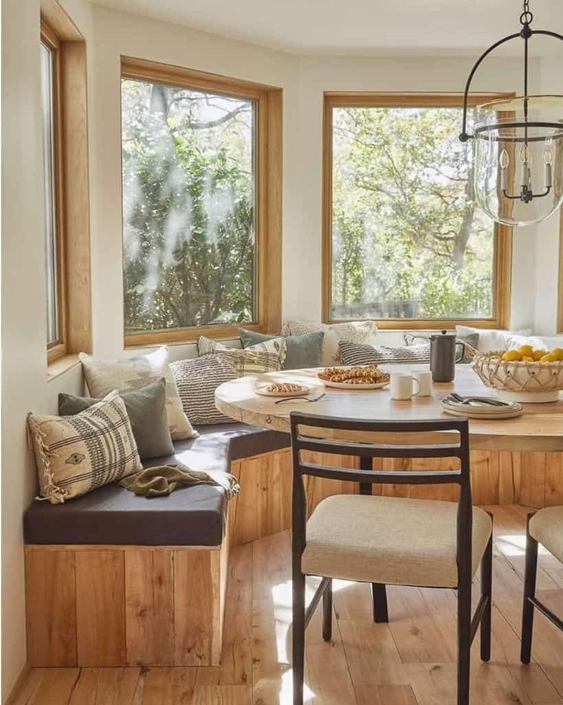 Warm and inviting bay window dining nook with a built-in wooden bench, cozy cushions, and a round table, perfect for relaxed gatherings.