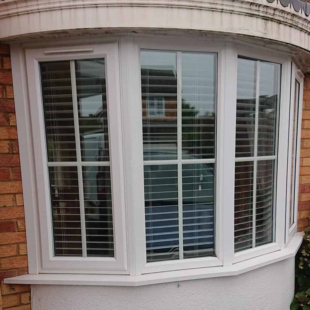 White bay window with classic grid-style panes and fitted blinds, offering privacy while allowing natural light to filter through.