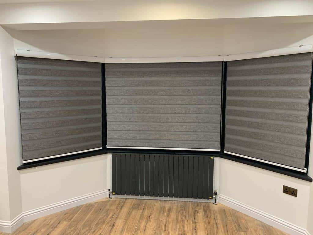 Modern bay window with sleek gray blackout blinds, a black radiator, and wood flooring, creating a stylish and functional space.