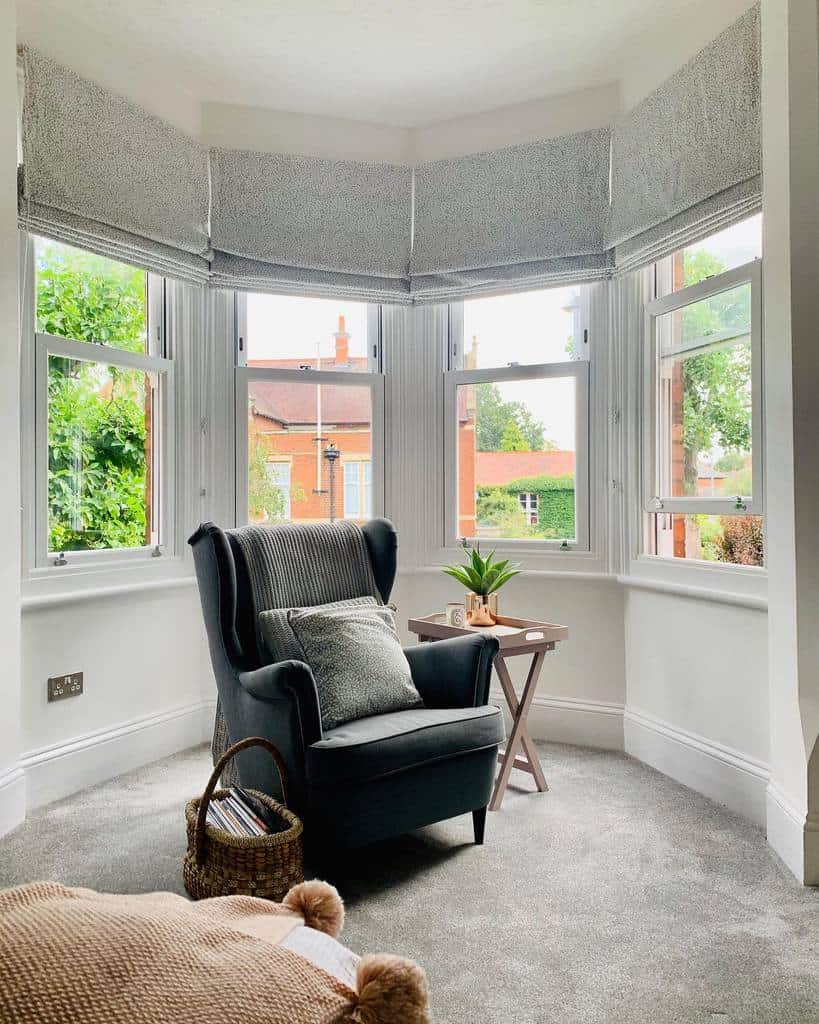 Cozy bay window reading nook with soft Roman blinds, a plush armchair, and a side table, creating a tranquil space to unwind.