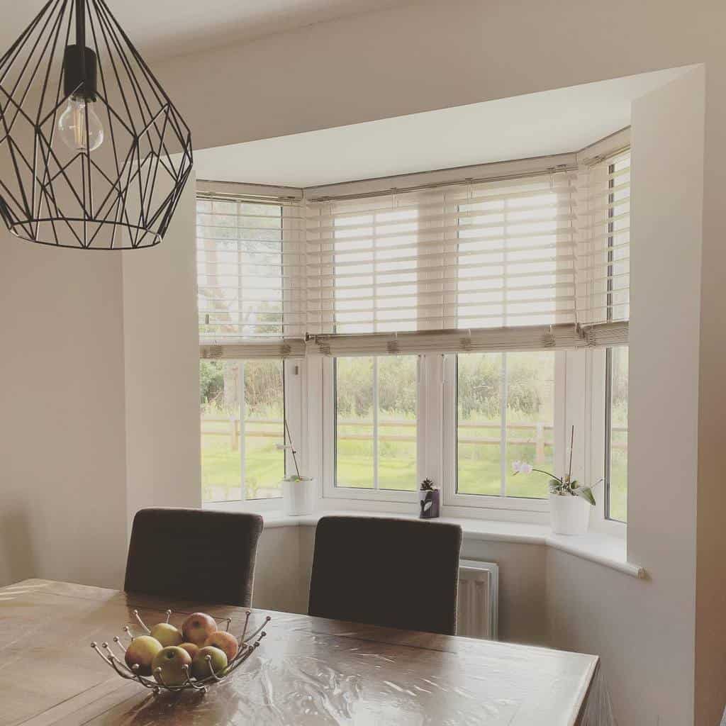 Bright dining area with a bay window, white wooden blinds, and a modern pendant light, offering a cozy yet stylish space with natural views