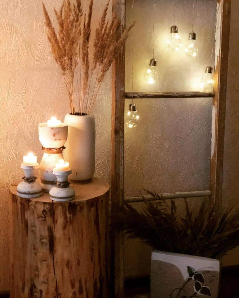 Repurposed old window frame decorated with hanging fairy lights, paired with rustic candles, pampas grass, and a wooden side table.