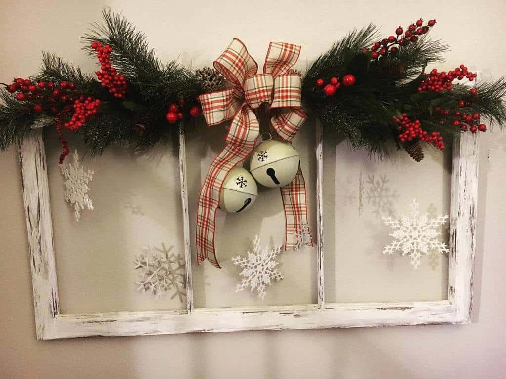 Repurposed old window frame decorated with festive garland, plaid ribbon, jingle bells, and snowflake accents for a Christmas touch.