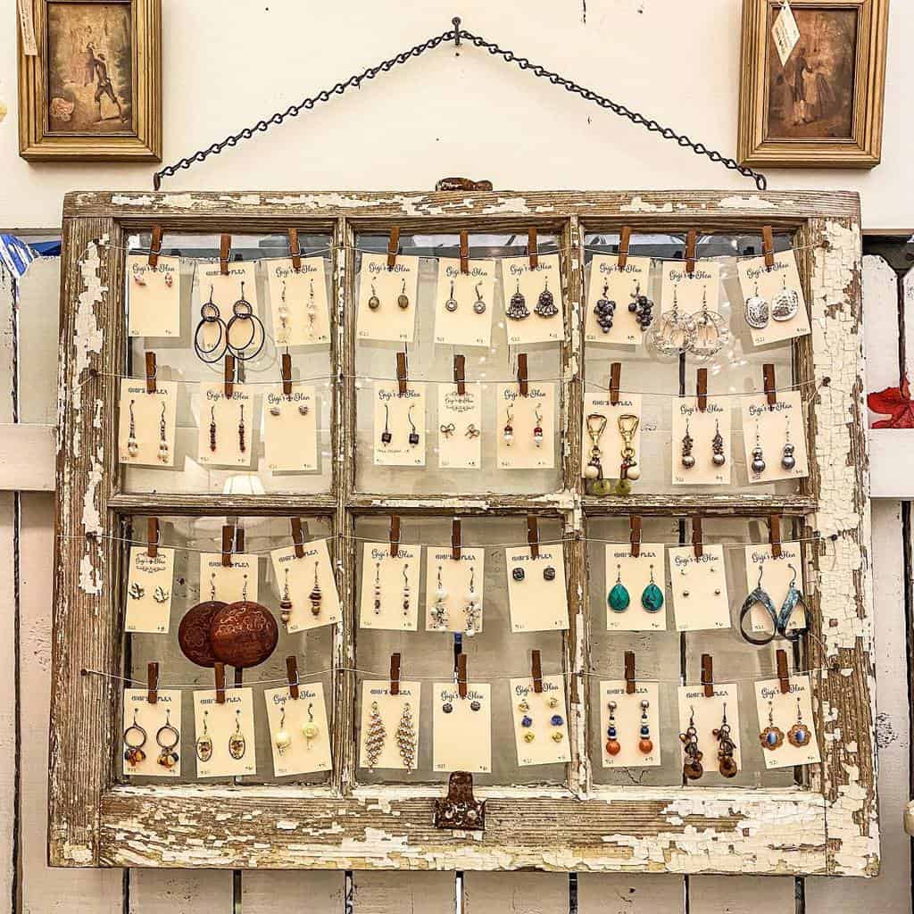 Rustic old window frame repurposed into a jewelry display, featuring earrings clipped to strings with mini clothespins.