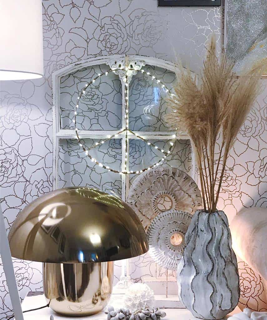 Repurposed arched window with a peace sign made of fairy lights, styled with a gold lamp, textured vase, and pampas grass.