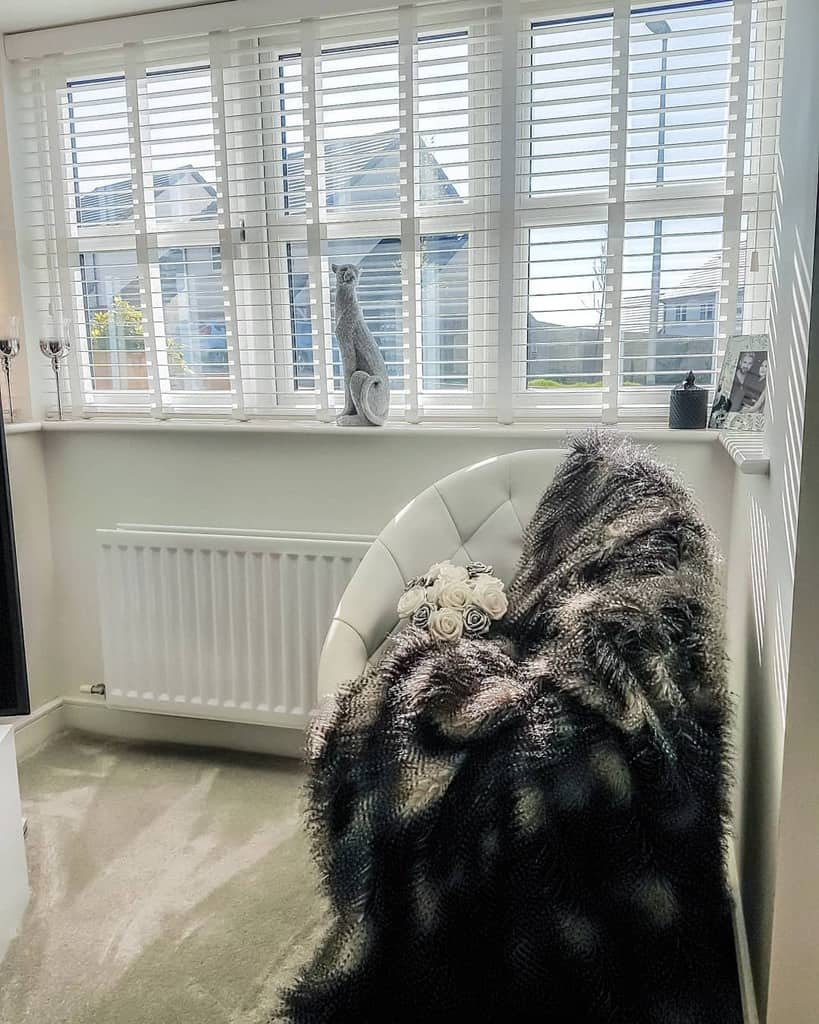 Elegant bay window nook with white wooden blinds, a plush fur throw, and a modern curved chair, creating a cozy and sophisticated retreat.