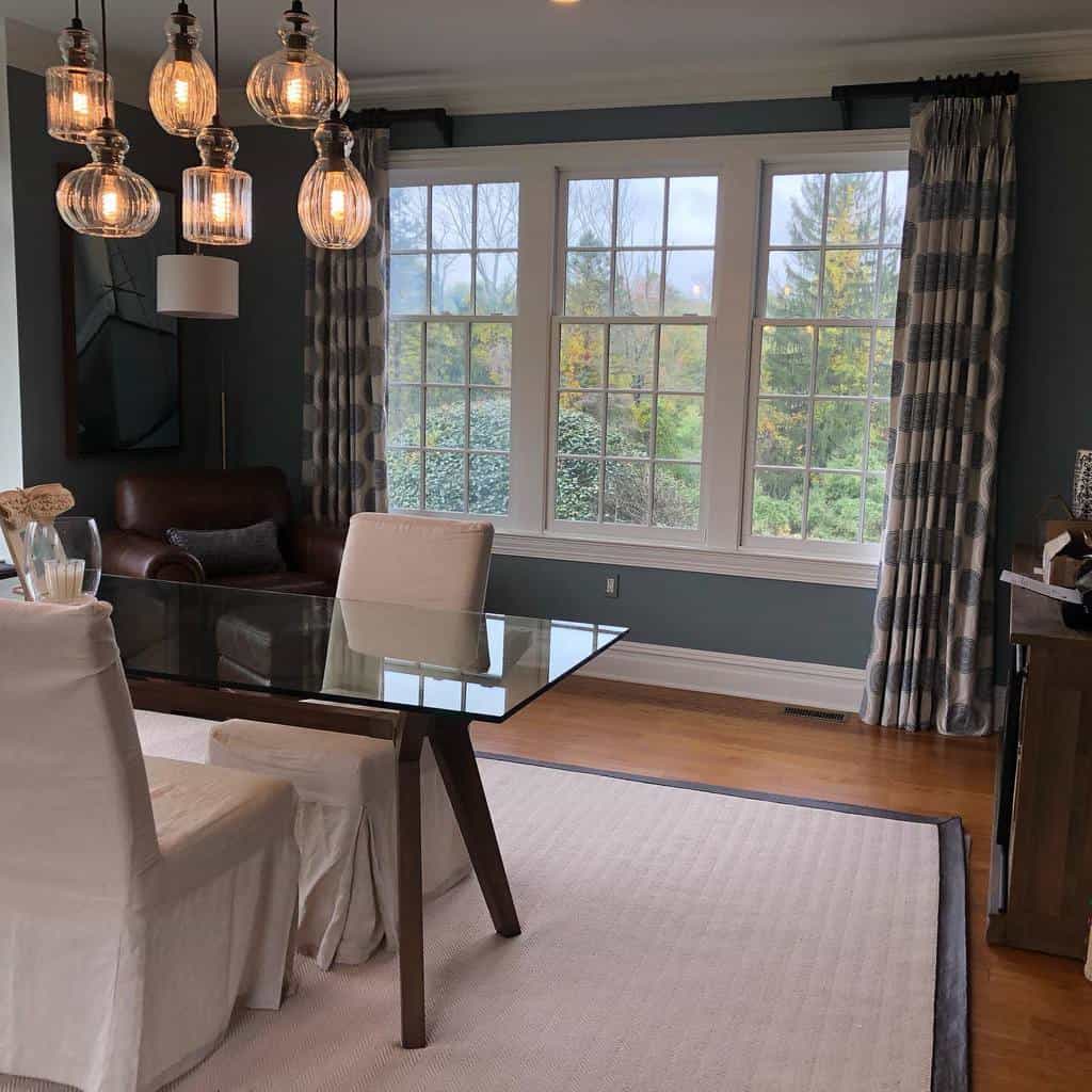 Elegant dining area with a bay window, patterned curtains, a glass-top table, and warm lighting, creating a cozy yet sophisticated ambiance.