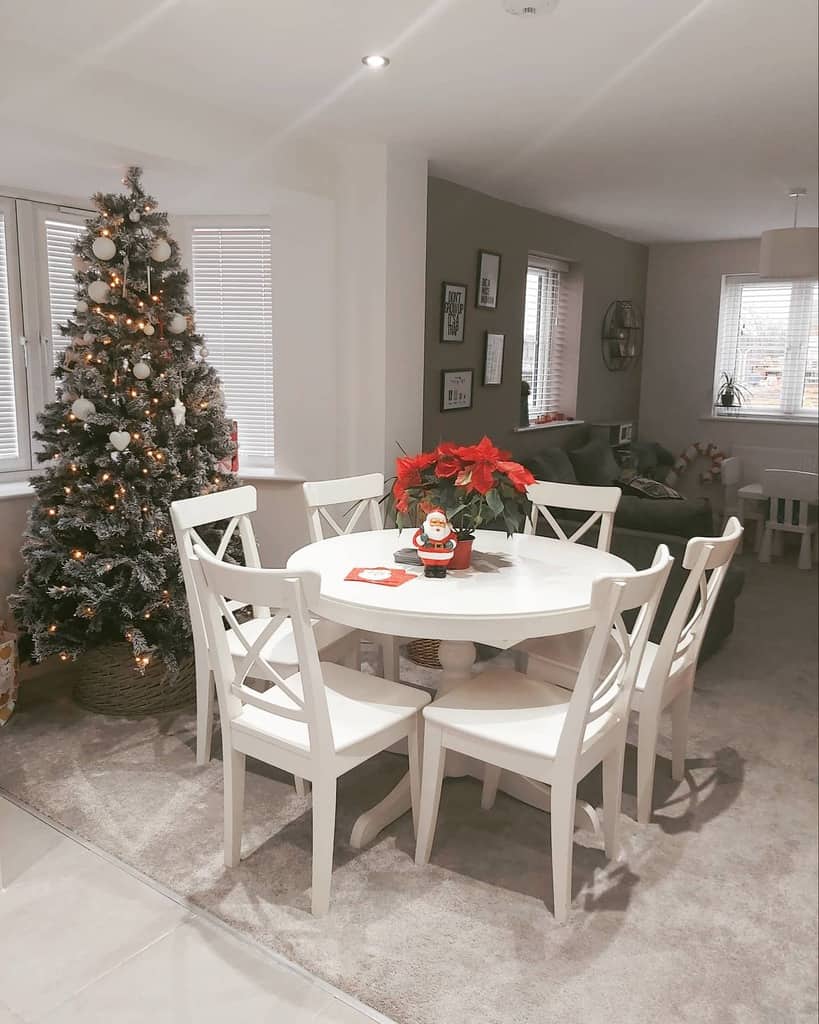 Festive dining area with a bay window, white wooden table and chairs, a decorated Christmas tree, and cozy holiday decor for a warm ambiance.