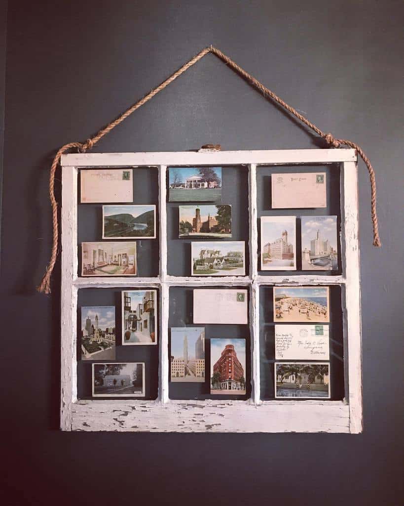 Vintage window frame repurposed as a postcard display, featuring old travel postcards and letters, hung with rustic rope on a dark wall.