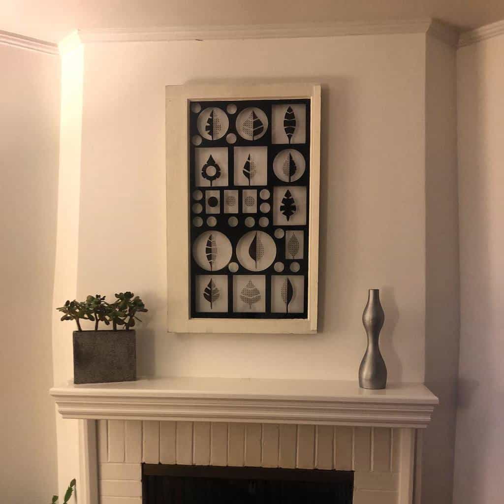 Repurposed old window frame turned into modern geometric wall art, featuring black and white leaf patterns, displayed above a fireplace.