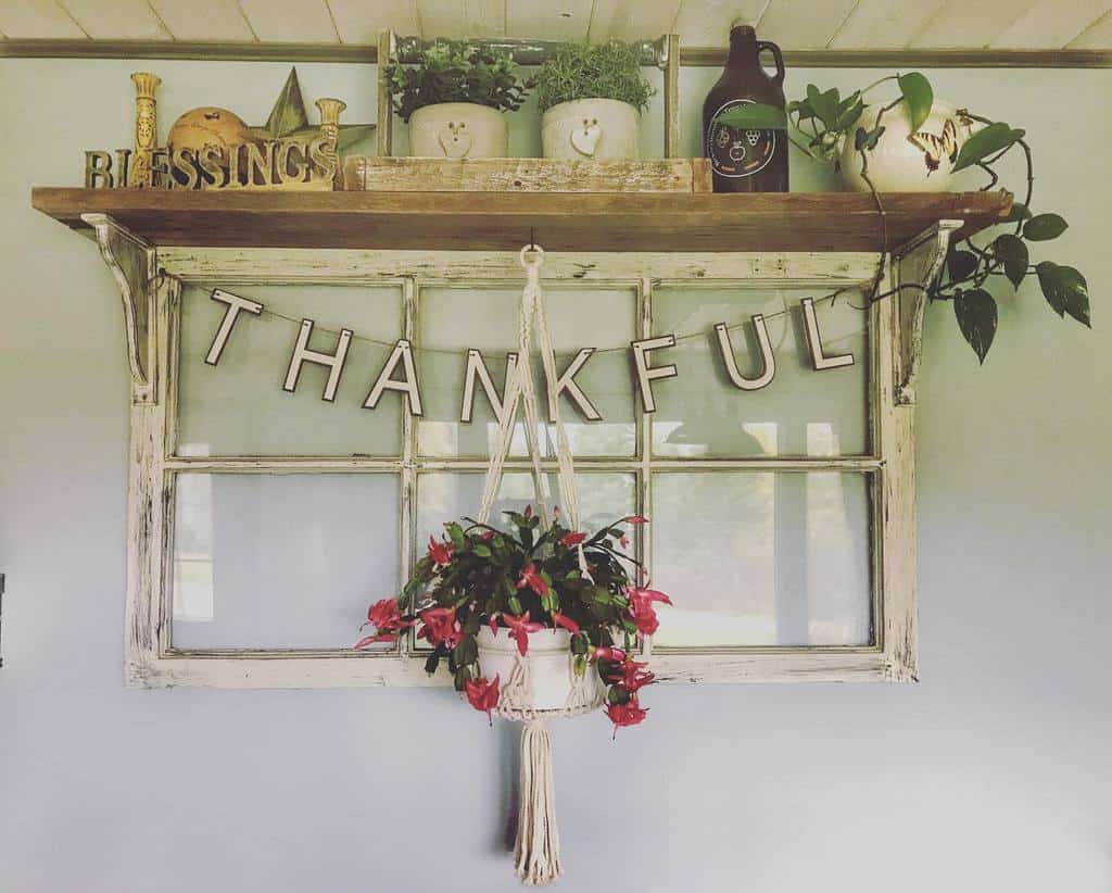 Repurposed old window frame with a 'Thankful' banner, a macrame hanging plant, and a rustic wooden shelf decorated with greenery.