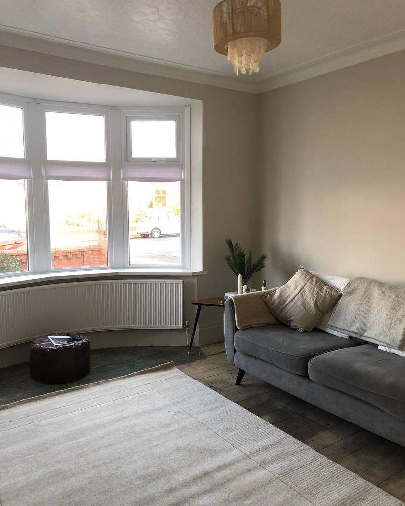 Minimalist living area with a bay window, soft Roman blinds, a cozy gray sofa, and natural wood flooring for a calm and airy feel.