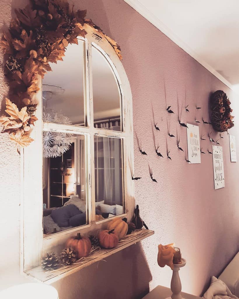 Repurposed arched window turned into a mirror, decorated with autumn leaves, pumpkins, and pinecones for a cozy seasonal display.