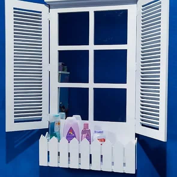 White faux window mirror with shutters and a picket fence-style shelf, mounted on a blue wall and used for bathroom storage.