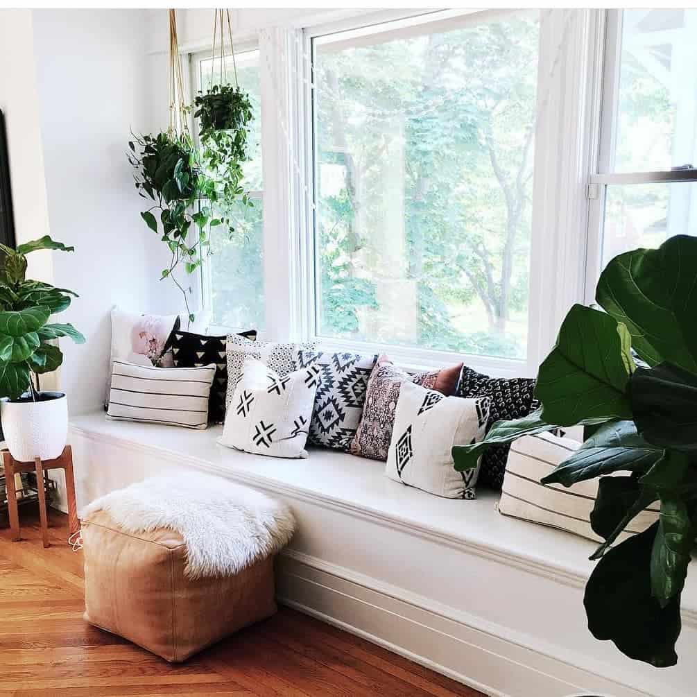 Boho-inspired bay window nook with a built-in bench, layered cushions, hanging plants, and natural light, creating a cozy and inviting retreat.