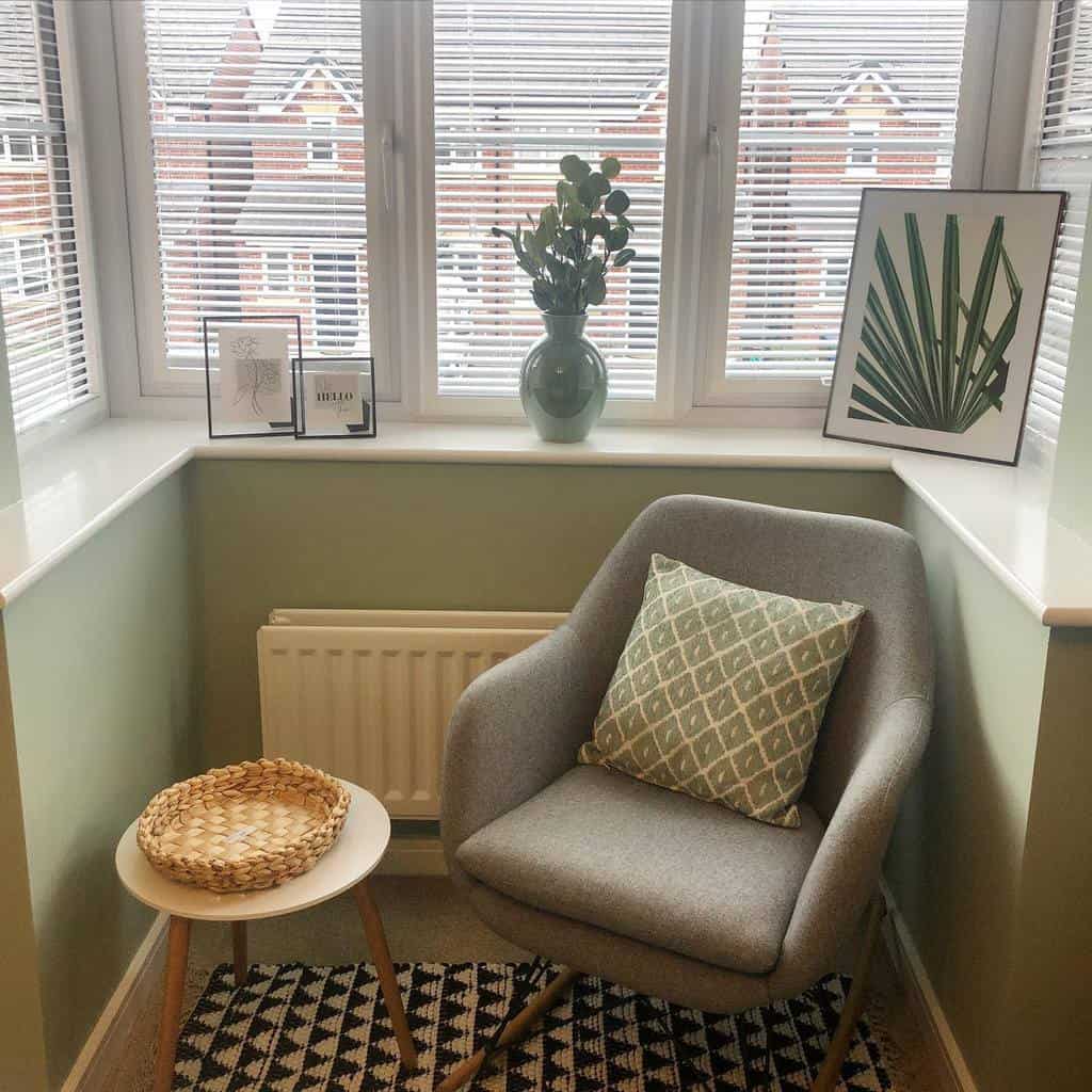 Modern bay window reading nook with a cozy gray chair, soft green walls, minimalist decor, and natural light, creating a serene relaxation spot.