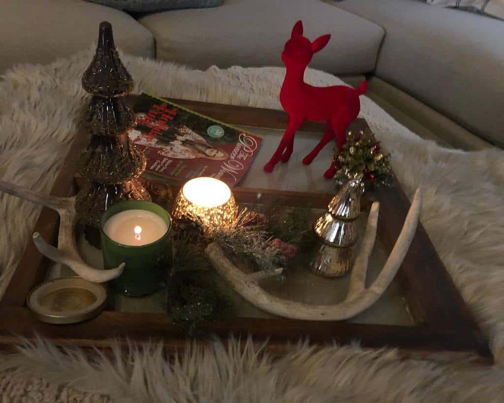 Repurposed old window frame used as a festive tray, decorated with candles, a red reindeer figurine, glass trees, and antlers for a cozy holiday display.