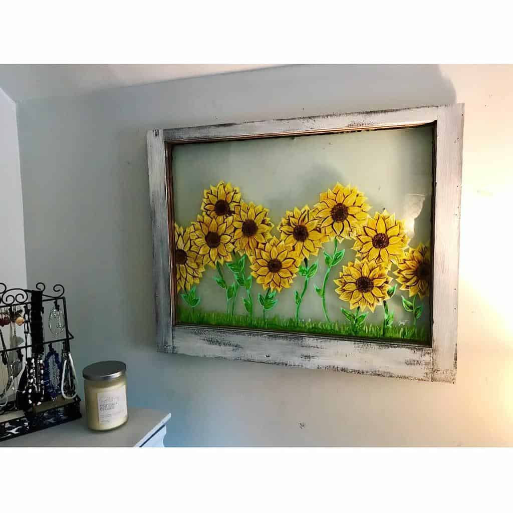 Repurposed old window frame with a distressed white finish, featuring hand-painted sunflowers on glass for a charming farmhouse wall decor.