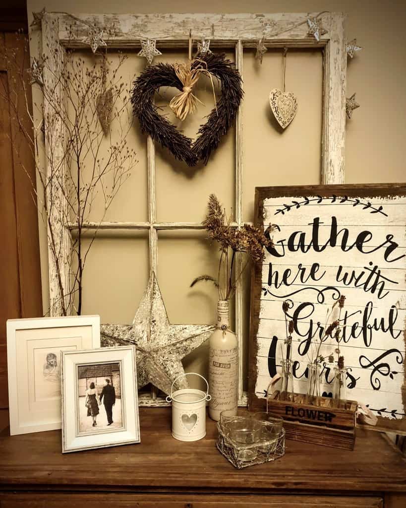 Rustic shabby chic display featuring a distressed old window frame, heart wreath, vintage decor, framed photos, and farmhouse-style accents.