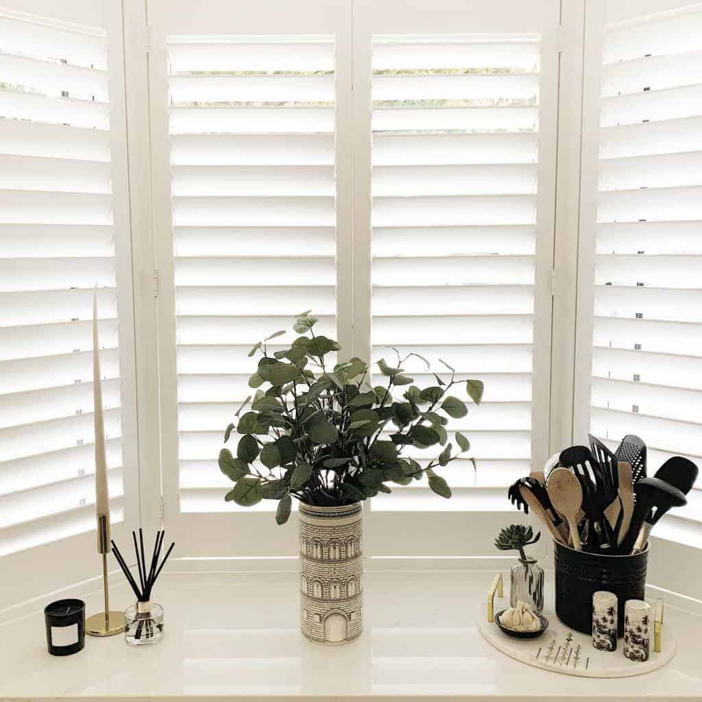 Minimalist bay window with white plantation shutters, elegant decor, and a stylish centerpiece, creating a bright and sophisticated space.