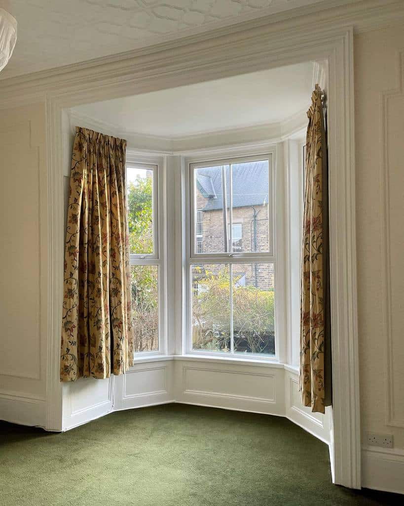 Classic bay window with floral curtains, white trim, and natural light, offering a charming and elegant space with vintage appeal.