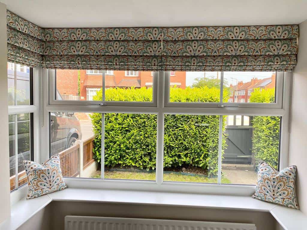 Charming square bay window with patterned Roman blinds, matching cushions, and a bright, airy view, creating a cozy and stylish nook.