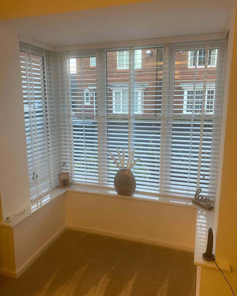 Bright square bay window with white blinds, a simple vase centerpiece, and a cozy ledge, creating a minimalist and inviting space.