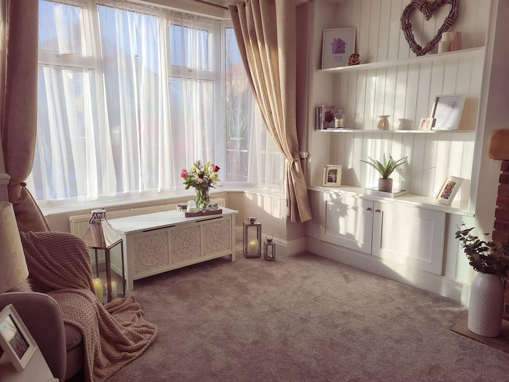 Cozy bay window nook with soft sheer curtains, warm neutral tones, built-in shelves, and elegant decor, creating a bright and inviting space.