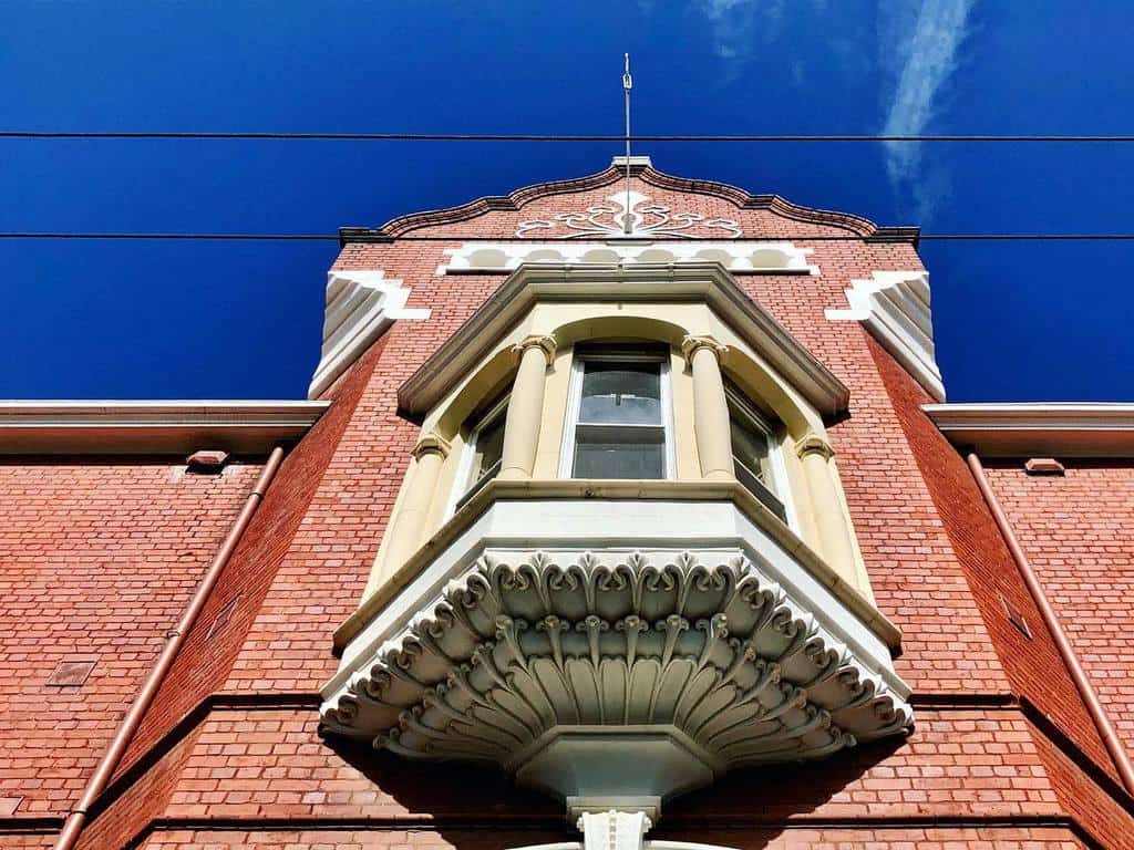 Ornate Victorian bay window with intricate stone detailing, set against a red brick facade, showcasing classic architectural elegance.