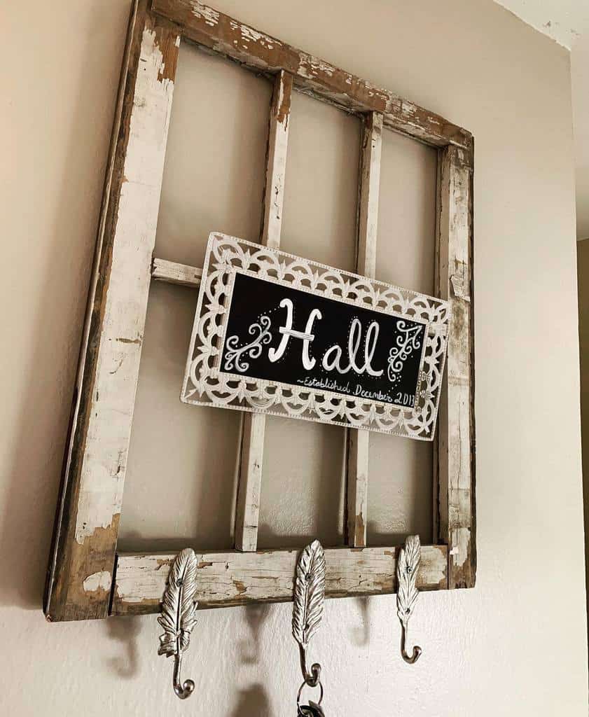 Repurposed old window frame turned into a rustic wall organizer with decorative feather hooks and a personalized chalkboard sign.