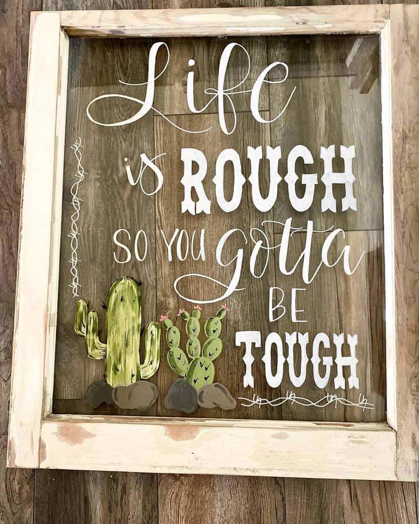 Rustic repurposed old window frame with hand-painted cactus art and an inspiring quote reading, 'Life is rough, so you gotta be tough.'