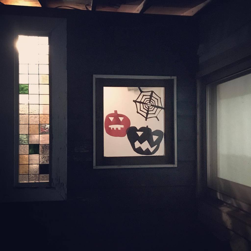 Repurposed old window decorated with Halloween-themed paper cutouts of jack-o'-lanterns and a spider web, illuminated in a dark rustic setting.