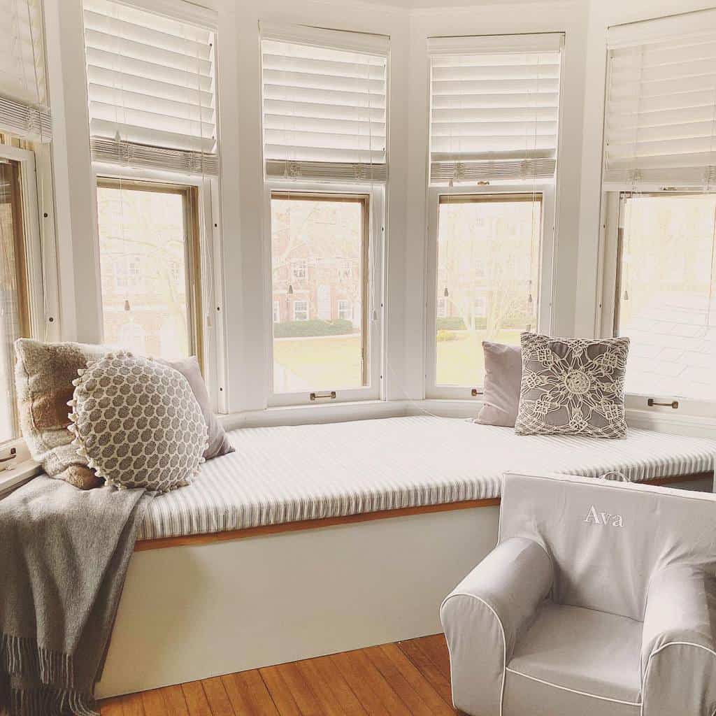 Bright and cozy bay window nook with a cushioned window seat, soft neutral-toned pillows, and warm natural light, creating a perfect reading spot.