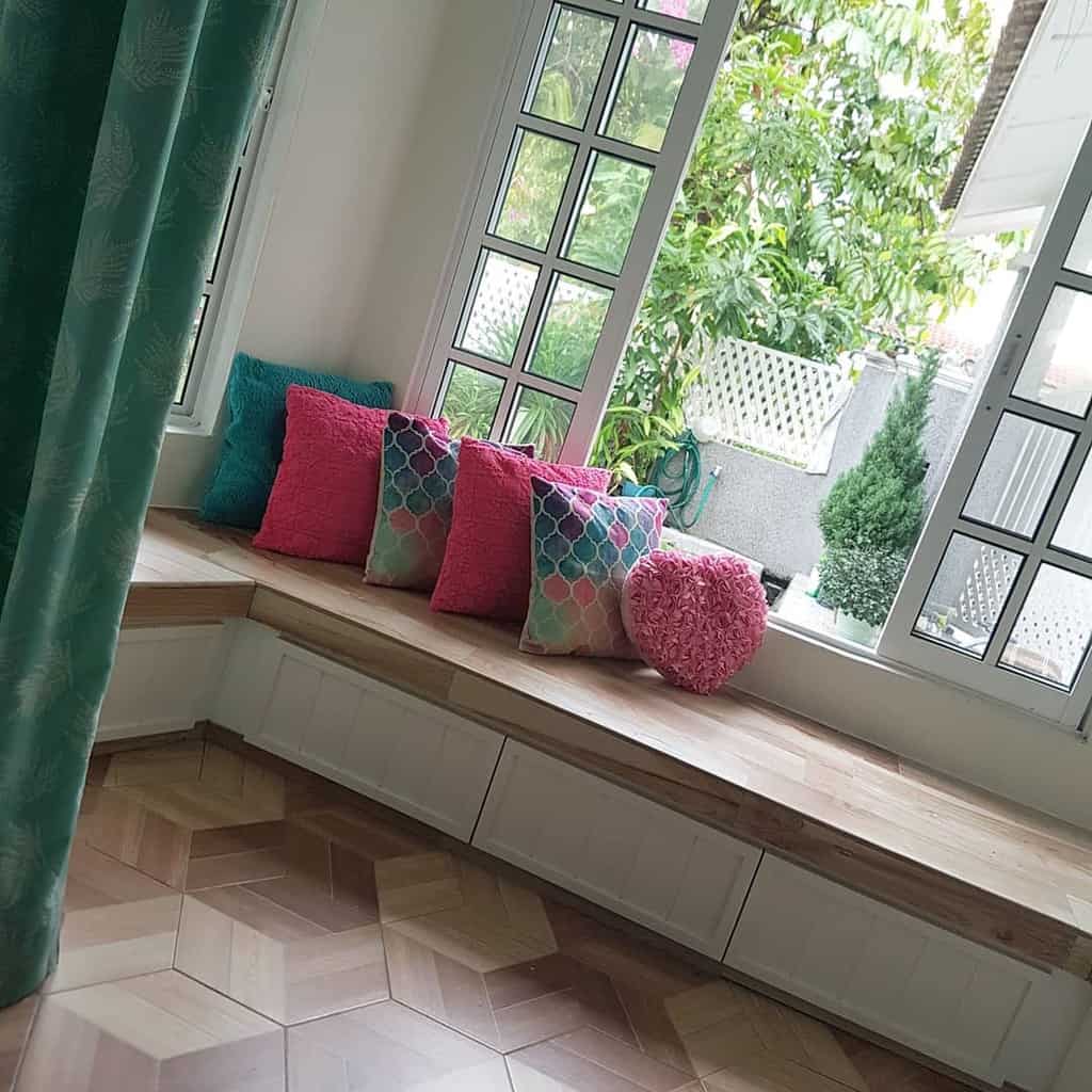 Charming bay window nook with a built-in wooden bench, colorful throw pillows, and lush greenery outside, creating a cozy and inviting space.