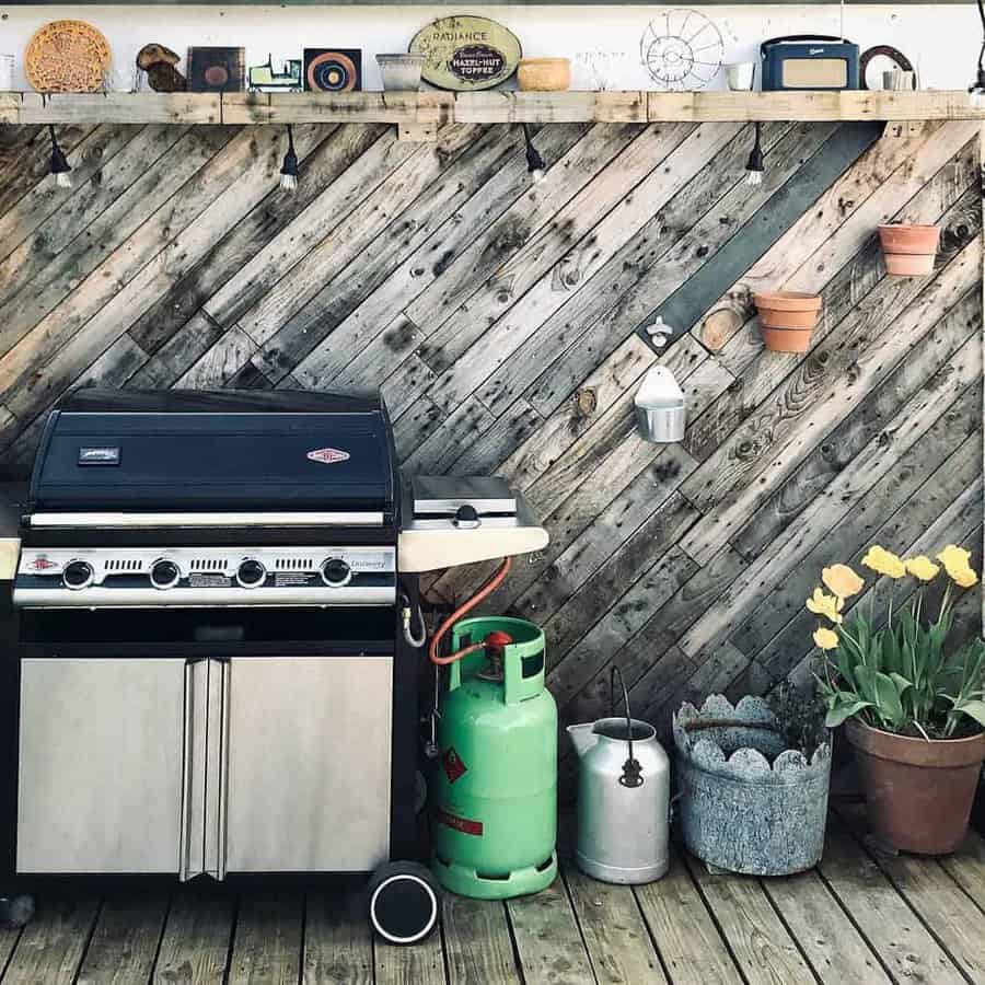 Outdoor patio with a gas grill, propane tank, potted tulips, and a rustic wooden pallet backdrop with hanging planters and decorations