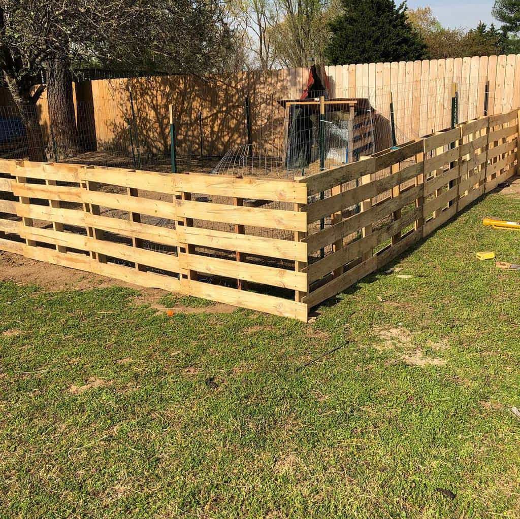 Sturdy DIY pallet fence enclosing a chicken coop, reinforced with wire mesh for a secure and budget-friendly backyard setup