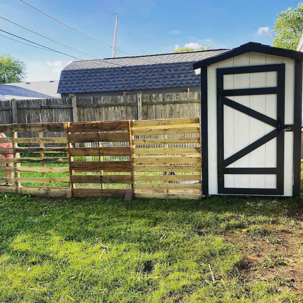 DIY pallet fence beside a black-and-white shed, creating a rustic and budget-friendly backyard enclosure with a natural wood finish