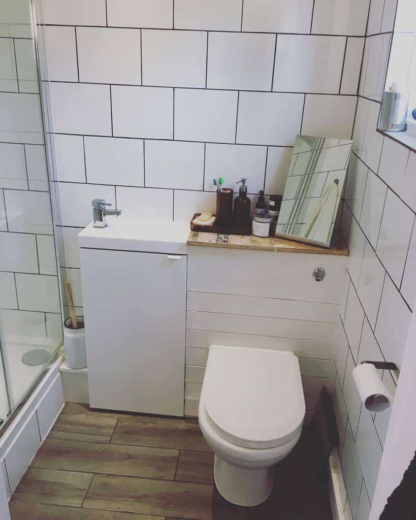 Compact bathroom with white subway tiles, a floating toilet, and a slim vanity. A wooden shelf adds warmth and storage space.