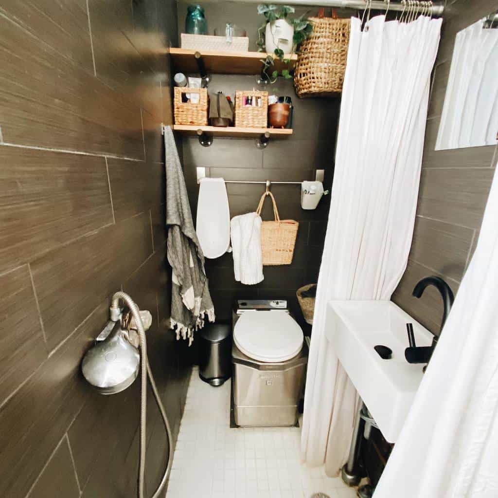 Compact bathroom showcasing small spaces design ideas with dark tiles, white shower curtain, small sink, overhead shower, and plant-filled shelves.