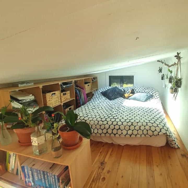 Cozy attic bedroom with a polka dot bedspread, houseplants, and bookshelves showcases smart small spaces design ideas. Bright window light fills the space.