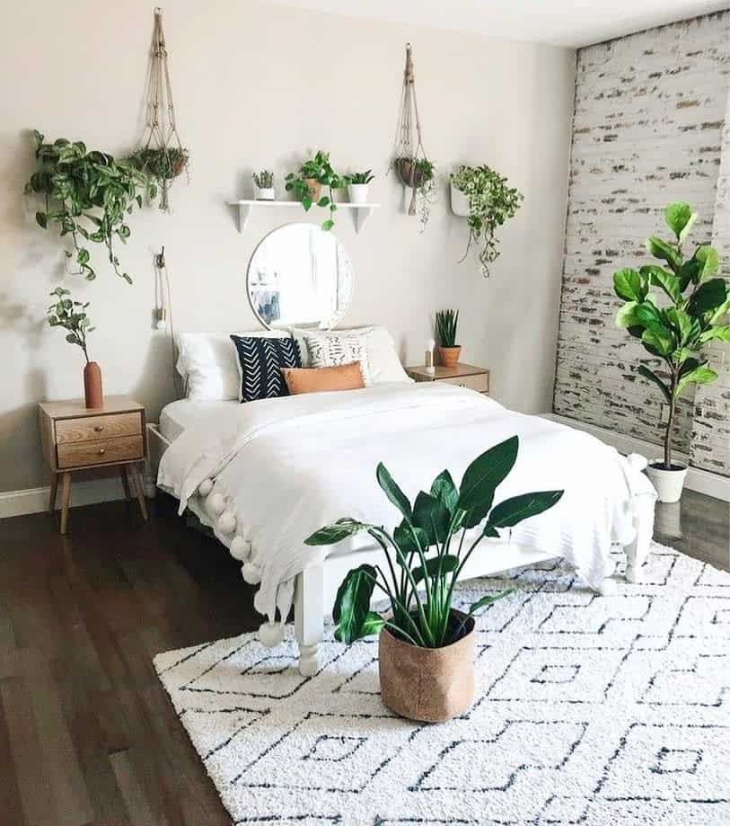 A cozy bedroom perfect for small spaces, featuring a white bed, plants, wood nightstands, geometric rug, and a brick accent wall.