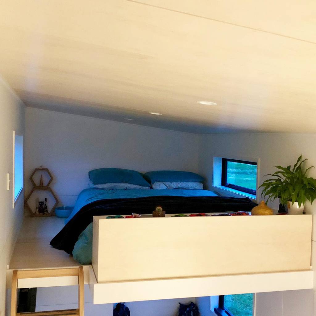 Cozy loft bedroom with slanted ceiling, blue bedding, small windows, and decorative shelves with plants.