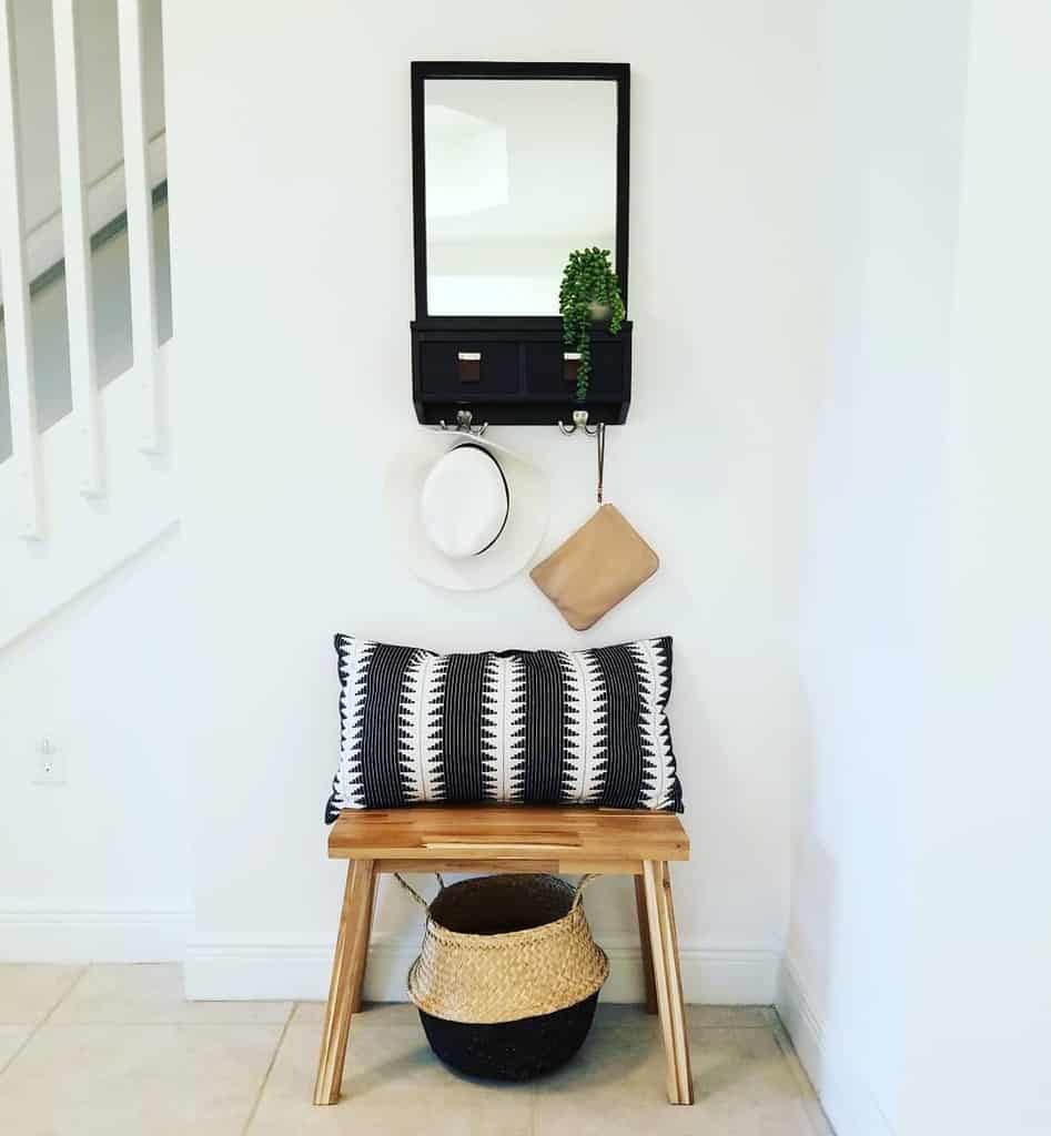 Modern entryway with a wooden bench, black and white accent pillow, wall-mounted mirror with storage, and a woven basket for organization