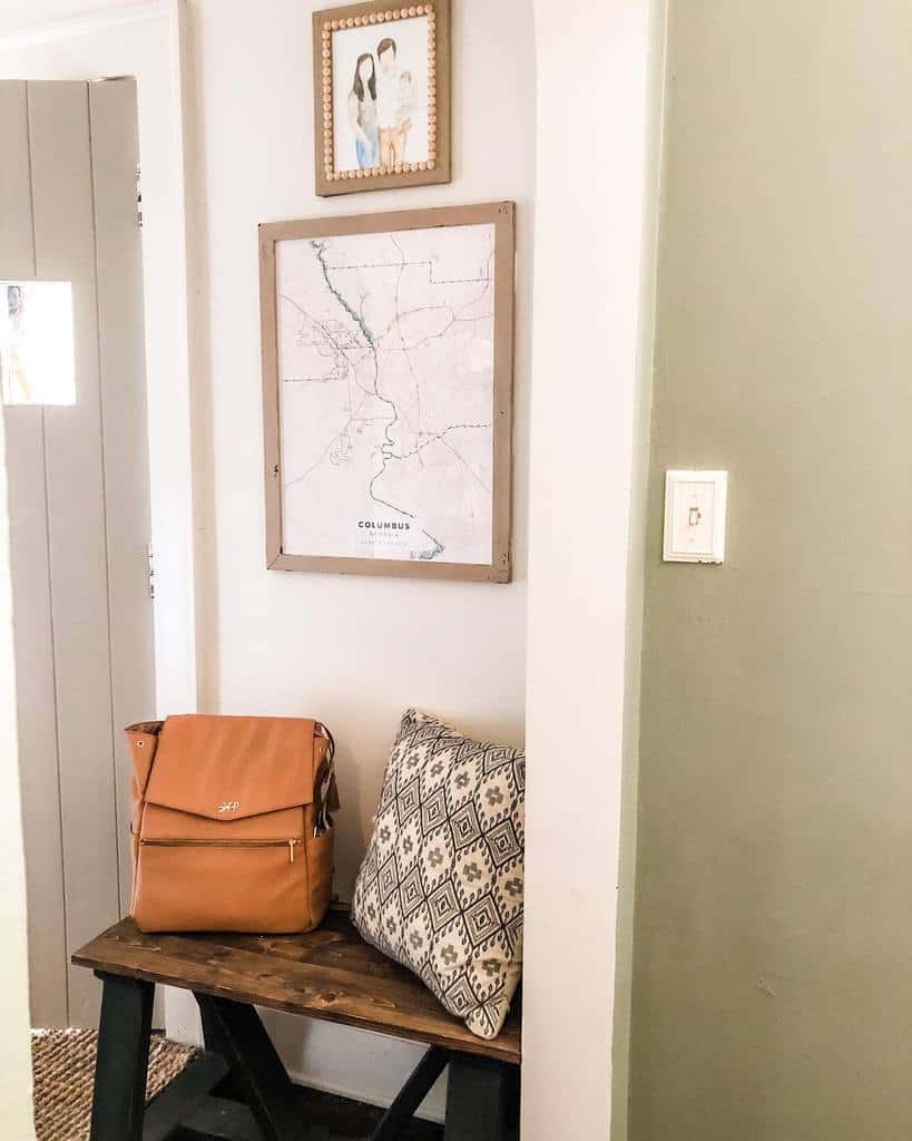 Rustic entryway with a dark wooden bench, patterned pillow, leather bag, framed city map, and cozy decor for a welcoming touch