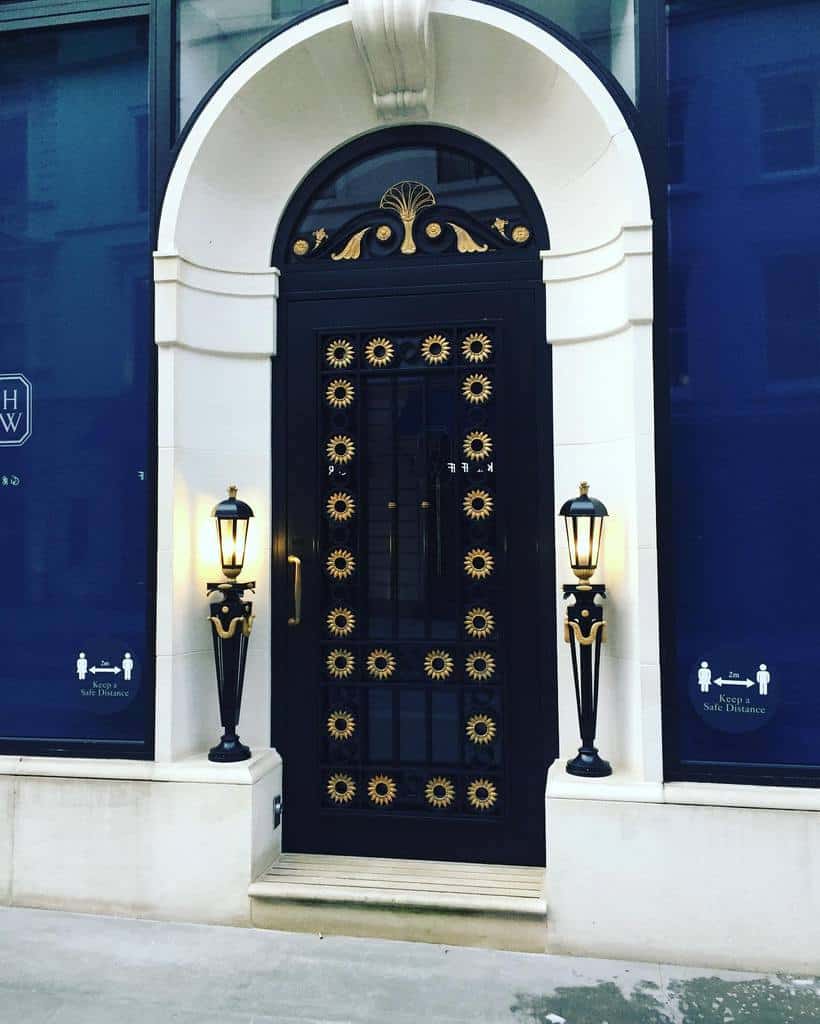 Elegant black door with gold sunburst designs, flanked by tall lanterns on a white stone facade