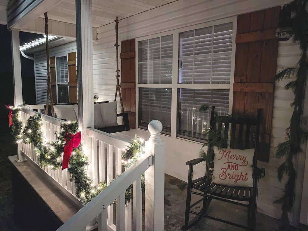 Cozy porch with a rocking chair, "Merry and Bright" pillow, festive garland with lights and red bows on the railing