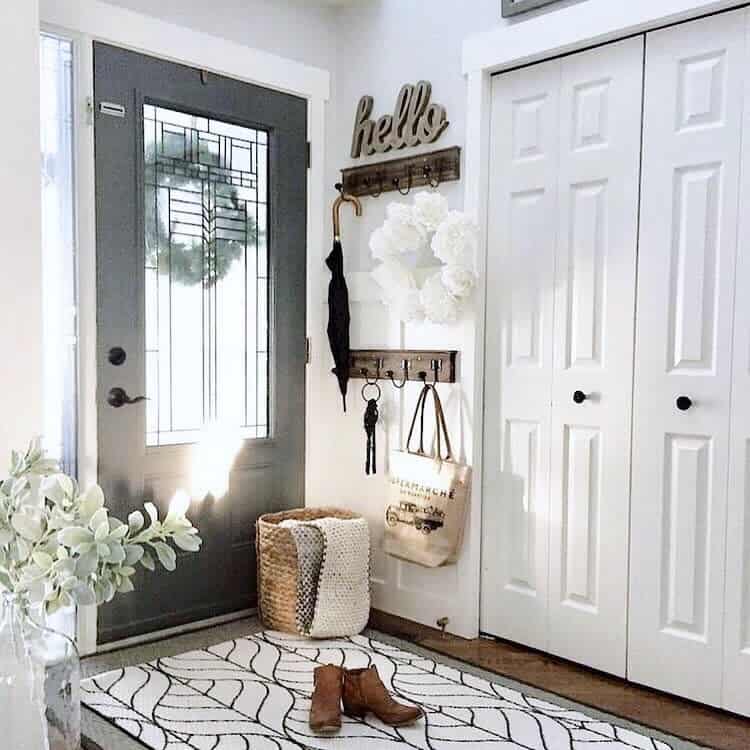 Bright and welcoming entryway with a black door, coat hooks, a woven storage basket, a patterned rug, and stylish decor accents