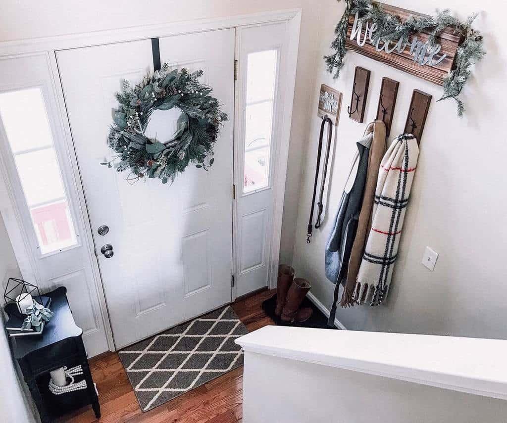 Cozy winter entryway with a festive wreath, wooden coat hooks, a plaid scarf, and a welcoming sign decorated with greenery