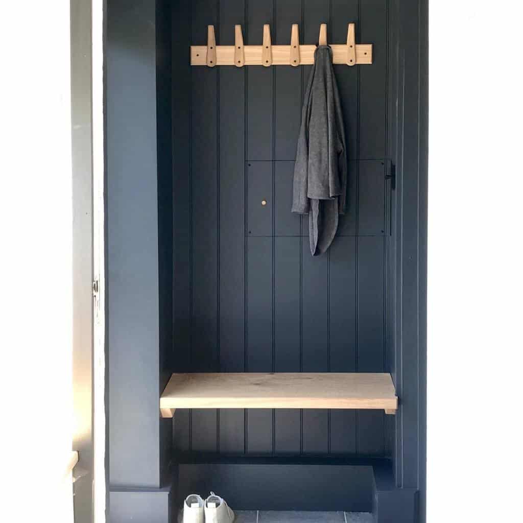 Minimalist entryway nook with dark paneled walls, a wooden bench, modern peg hooks, and a simple coat storage solution